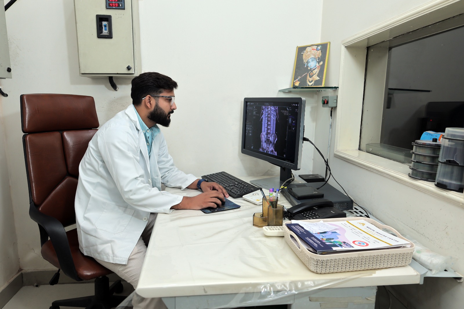 Technician operating the controls of a GE MRI machine with a patient inside.