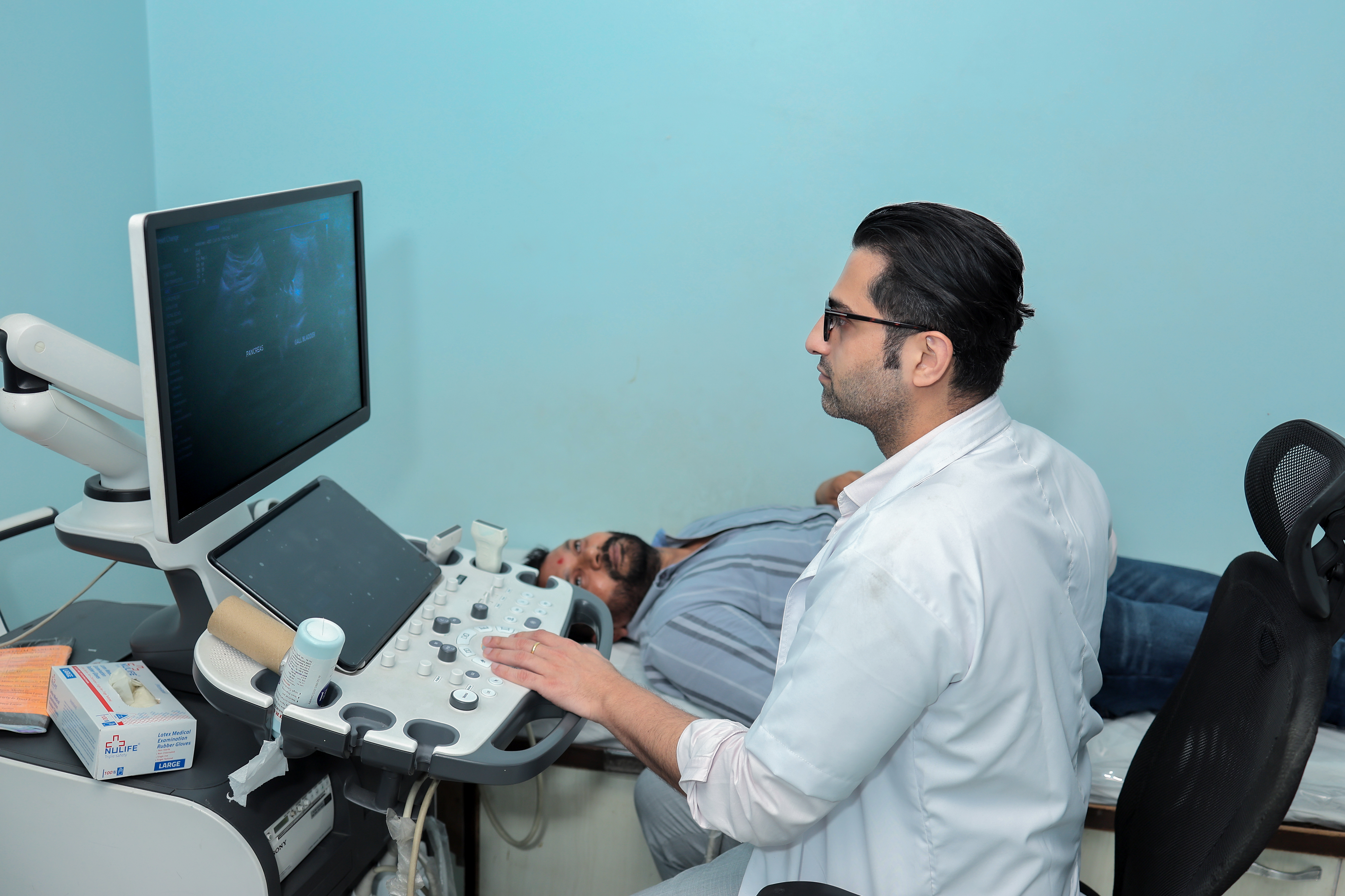Technician operating the controls of a GE MRI machine with a patient inside.